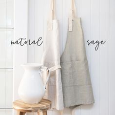 two aprons are hanging on the wall next to a white vase and wooden stool