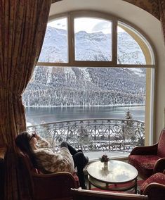 a woman laying on top of a couch in front of a window next to a table