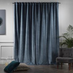 a living room filled with furniture and a large window covered in blue drapes next to a chair