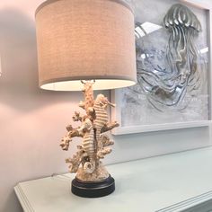 a lamp that is sitting on top of a dresser next to a painting and seahorse