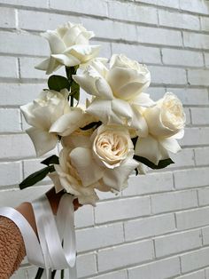 a bouquet of white roses in front of a brick wall with someone's hand holding it