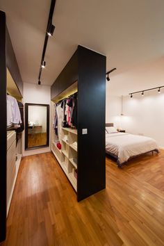 an open closet in a bedroom with wooden floors and white walls, filled with clothes