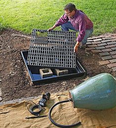 a man working on a drain in the ground with a hose connected to it and a grate next to it