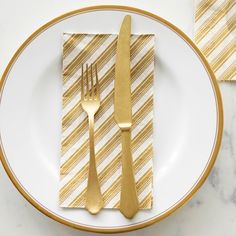 a white plate topped with two gold colored forks and a napkin on top of it