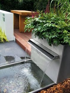 a water fountain in the middle of a garden with plants growing on it's sides