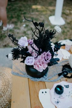 a black vase filled with lots of flowers on top of a wooden table next to other items