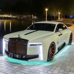 a white rolls royce parked in front of a lake at night