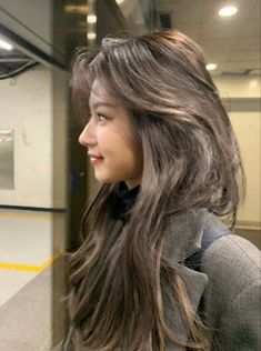 a woman with long brown hair standing in front of a train door and looking off into the distance