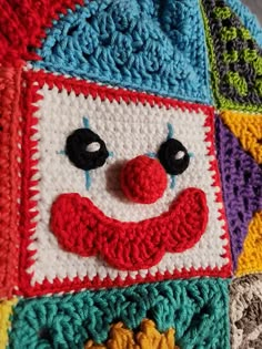 a crocheted clown face on top of a colorful blanket that is made to look like it's smiling