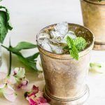 two glasses filled with ice and mint on top of a table next to some flowers