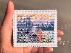 a hand holding up a small cross stitched stamp with a castle in the background