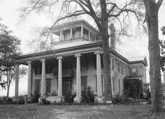 black and white photograph of an old house with columns on the front porch, surrounded by trees