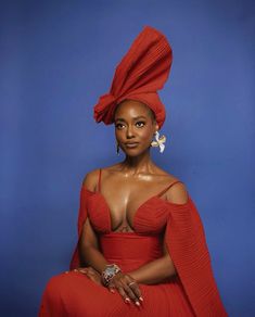 an african woman in a red dress and headdress sitting on a blue background