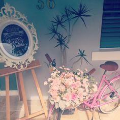 a pink bicycle parked next to a table with flowers in it and a mirror on the wall