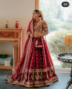 a woman in a red and gold bridal gown standing next to a table with a lamp