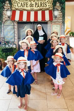 a group of children wearing hats and capes in front of a cafe de paris