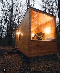 a small wooden cabin in the woods at night with lights shining on it's windows