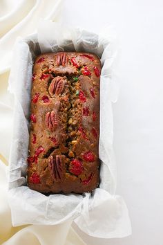 a loaf of fruit bread sitting in a paper wrapper on top of a white cloth