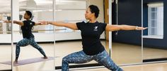 two women doing yoga poses in front of mirrored walls, one with her arms stretched out