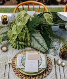 a table set with plates, silverware and greenery