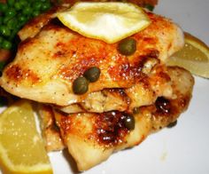 a white plate topped with chicken, peas and lemon wedges next to broccoli