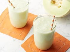 two glasses filled with green smoothie sitting on top of orange napkins next to an apple