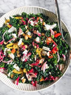 a white bowl filled with salad on top of a marble table next to a fork