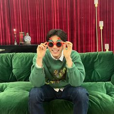 a man sitting on top of a green couch holding up sunglasses to his eyeglasses