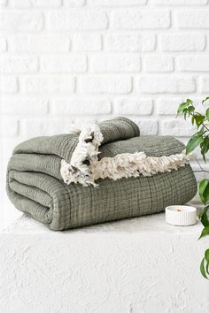 two folded towels sitting on top of each other next to a potted plant and a white brick wall