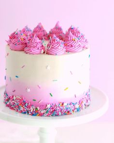 a white cake with pink frosting and sprinkles on a plate against a pink background