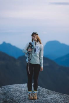 a woman standing on top of a mountain holding a camera