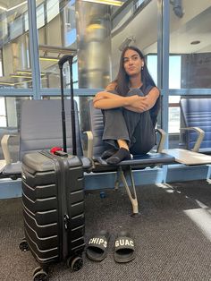 a woman sitting on an airport bench with her suitcase and shoes next to her feet