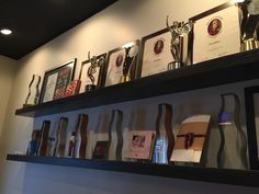 many trophies are on the shelves in front of pictures and framed photographs, along with other awards