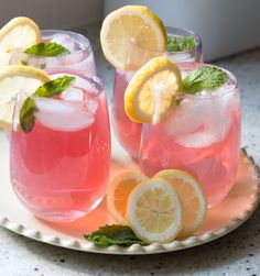 three glasses filled with pink lemonade and mint sprits on a white plate