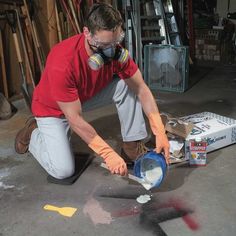 a man in a red shirt and mask painting on the floor with paint rollers