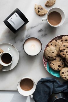 two cups of coffee and some cookies on a marble table with a bottle of wine