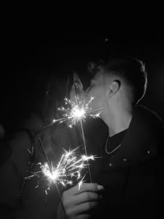 two people kissing and holding sparklers in their hands, black and white photo with dark background