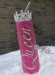 a pink can with a crown on top of it sitting in the snow next to a brick wall