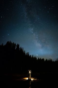 a man and woman standing in the middle of a field under a night sky filled with stars