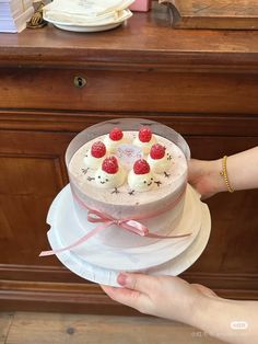 a person holding a cake with raspberries on top and white frosting in the middle