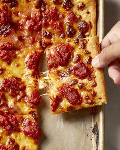 a person taking a slice of pepperoni pizza from a metal pan on a table