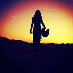 the silhouette of a woman walking in front of a sunset