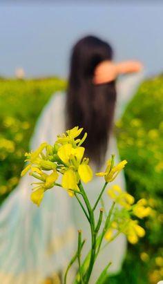 a woman with long black hair is standing in a field full of yellow flowers and holding her hand out to the side