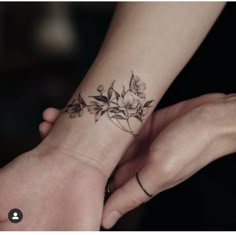 two hands holding each other with tattoos on their wrist and one has a flower tattoo on it