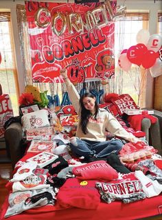 a woman sitting on top of a bed covered in red and white shirts with balloons