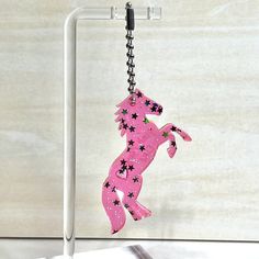 a pink horse shaped keychain hanging from a metal hook on a white stand