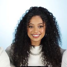 a woman with long curly hair smiling and wearing a white shirt in front of a blue background