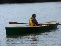 an older man in a yellow life jacket paddling a green canoe on the water