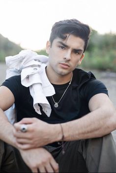 a young man sitting on the ground with his hands folded over his chest and looking at the camera