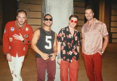 three men standing next to each other in front of a column wearing red pants and sunglasses